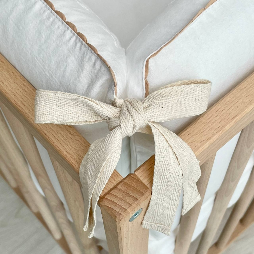 Detailaufnahme des süßen Bindebändchens, mit dem der Babybett-Bumper sicher am Bett befestigt wird, in passendem Milchweiß, das dem Set eine zarte und elegante Note verleiht